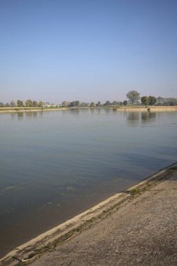 İtalya 'nın kırsal kesimlerinde güneşli bir günde ufuk çizgisi ve köprüsü olan küçük bir ada tarafından yapılan saptırıcı bir kanalda çatal.