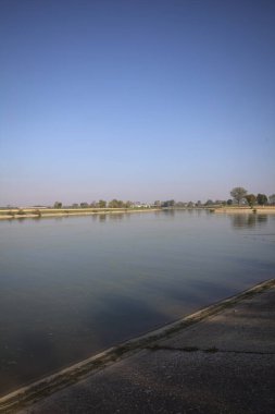 İtalya 'nın kırsal kesimlerinde güneşli bir günde ufuk çizgisi ve köprüsü olan küçük bir ada tarafından yapılan saptırıcı bir kanalda çatal.