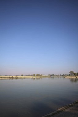 İtalya 'nın kırsal kesimlerinde güneşli bir günde ufuk çizgisi ve köprüsü olan küçük bir ada tarafından yapılan saptırıcı bir kanalda çatal.