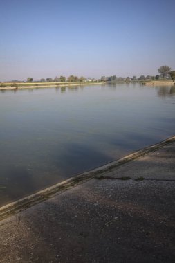 İtalya 'nın kırsal kesimlerinde güneşli bir günde ufuk çizgisi ve köprüsü olan küçük bir ada tarafından yapılan saptırıcı bir kanalda çatal.