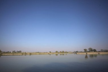 İtalya 'nın kırsal kesimlerinde güneşli bir günde ufuk çizgisi ve köprüsü olan küçük bir ada tarafından yapılan saptırıcı bir kanalda çatal.