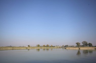 İtalya 'nın kırsal kesimlerinde güneşli bir günde ufuk çizgisi ve köprüsü olan küçük bir ada tarafından yapılan saptırıcı bir kanalda çatal.