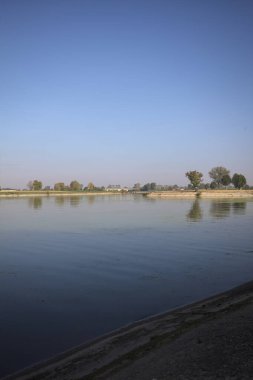 İtalya 'nın kırsal kesimlerinde güneşli bir günde ufuk çizgisi ve köprüsü olan küçük bir ada tarafından yapılan saptırıcı bir kanalda çatal.