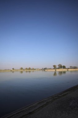 İtalya 'nın kırsal kesimlerinde güneşli bir günde ufuk çizgisi ve köprüsü olan küçük bir ada tarafından yapılan saptırıcı bir kanalda çatal.