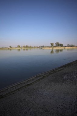 İtalya 'nın kırsal kesimlerinde güneşli bir günde ufuk çizgisi ve köprüsü olan küçük bir ada tarafından yapılan saptırıcı bir kanalda çatal.