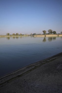 İtalya 'nın kırsal kesimlerinde güneşli bir günde ufuk çizgisi ve köprüsü olan küçük bir ada tarafından yapılan saptırıcı bir kanalda çatal.
