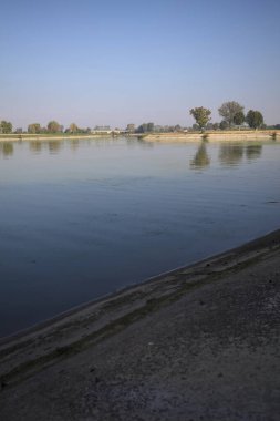 İtalya 'nın kırsal kesimlerinde güneşli bir günde ufuk çizgisi ve köprüsü olan küçük bir ada tarafından yapılan saptırıcı bir kanalda çatal.