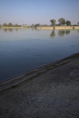 İtalya 'nın kırsal kesimlerinde güneşli bir günde ufuk çizgisi ve köprüsü olan küçük bir ada tarafından yapılan saptırıcı bir kanalda çatal.