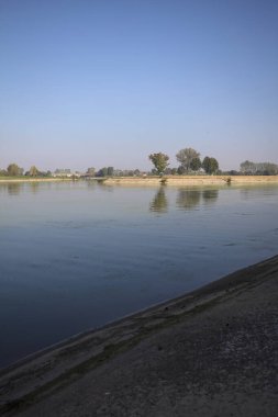 İtalya 'nın kırsal kesimlerinde güneşli bir günde ufuk çizgisi ve köprüsü olan küçük bir ada tarafından yapılan saptırıcı bir kanalda çatal.