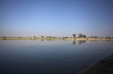İtalya 'nın kırsal kesimlerinde güneşli bir günde ufuk çizgisi ve köprüsü olan küçük bir ada tarafından yapılan saptırıcı bir kanalda çatal.
