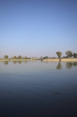 İtalya 'nın kırsal kesimlerinde güneşli bir günde ufuk çizgisi ve köprüsü olan küçük bir ada tarafından yapılan saptırıcı bir kanalda çatal.
