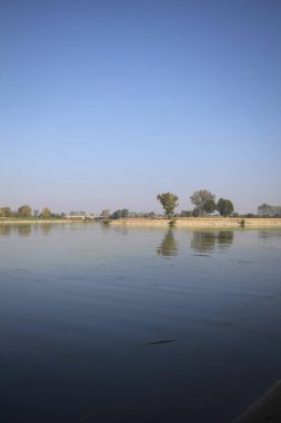 İtalya 'nın kırsal kesimlerinde güneşli bir günde ufuk çizgisi ve köprüsü olan küçük bir ada tarafından yapılan saptırıcı bir kanalda çatal.