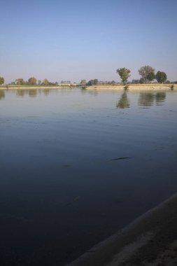 İtalya 'nın kırsal kesimlerinde güneşli bir günde ufuk çizgisi ve köprüsü olan küçük bir ada tarafından yapılan saptırıcı bir kanalda çatal.