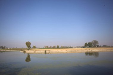 İtalya 'nın kırsal kesimlerinde güneşli bir günde ufuk çizgisi ve köprüsü olan küçük bir ada tarafından yapılan saptırıcı bir kanalda çatal.