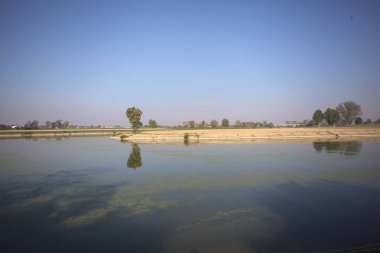 İtalya 'nın kırsal kesimlerinde güneşli bir günde ufuk çizgisi ve köprüsü olan küçük bir ada tarafından yapılan saptırıcı bir kanalda çatal.