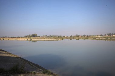 İtalya 'nın kırsal kesimlerinde güneşli bir günde ufuk çizgisi ve köprüsü olan küçük bir ada tarafından yapılan saptırıcı bir kanalda çatal.
