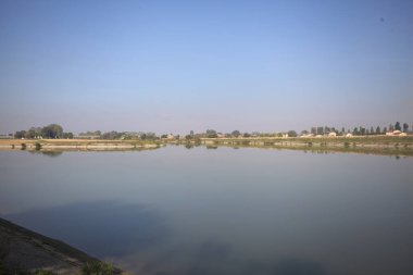 İtalya 'nın kırsal kesimlerinde güneşli bir günde ufuk çizgisi ve köprüsü olan küçük bir ada tarafından yapılan saptırıcı bir kanalda çatal.