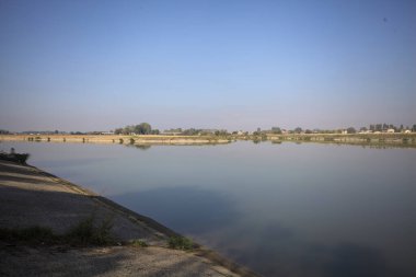 İtalya 'nın kırsal kesimlerinde güneşli bir günde ufuk çizgisi ve köprüsü olan küçük bir ada tarafından yapılan saptırıcı bir kanalda çatal.