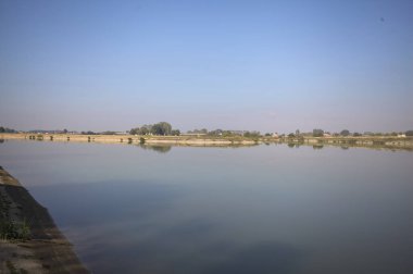 İtalya 'nın kırsal kesimlerinde güneşli bir günde ufuk çizgisi ve köprüsü olan küçük bir ada tarafından yapılan saptırıcı bir kanalda çatal.