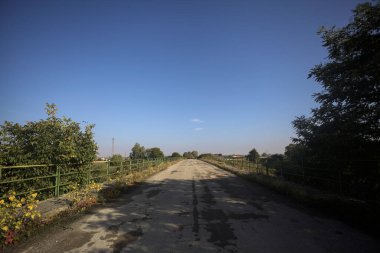 İtalya kırsalında güneşli bir günde, bir ucunda metalik korkuluklar olan yıpranmış bir köprü.