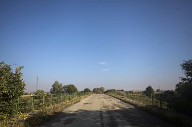 İtalya kırsalında güneşli bir günde, bir ucunda metalik korkuluklar olan yıpranmış bir köprü.