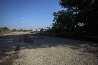 İtalya kırsalında güneşli bir günde, bir ucunda metalik korkuluklar olan yıpranmış bir köprü.