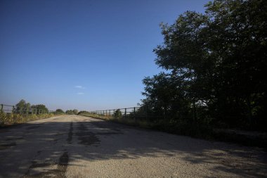 İtalya kırsalında güneşli bir günde, bir ucunda metalik korkuluklar olan yıpranmış bir köprü.