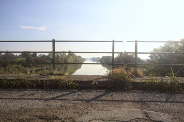 Nehir, üzerinde bir köprüden görünen suya yansıyan ağaçlarla çevrili güneşle kesişir.