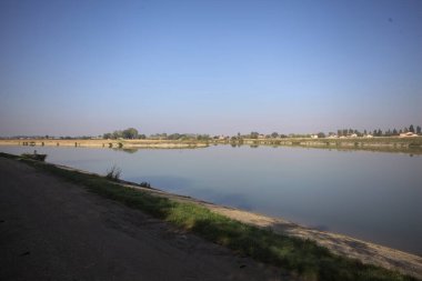 İtalya 'nın kırsal kesimlerinde güneşli bir günde ufuk çizgisi ve köprüsü olan küçük bir ada tarafından yapılan saptırıcı bir kanalda çatal.