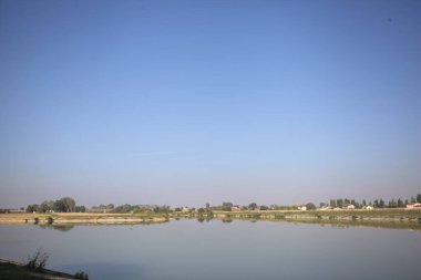 İtalya 'nın kırsal kesimlerinde güneşli bir günde ufuk çizgisi ve köprüsü olan küçük bir ada tarafından yapılan saptırıcı bir kanalda çatal.