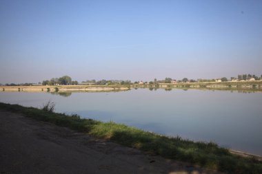 İtalya 'nın kırsal kesimlerinde güneşli bir günde ufuk çizgisi ve köprüsü olan küçük bir ada tarafından yapılan saptırıcı bir kanalda çatal.