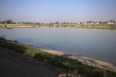 İtalya 'nın kırsal kesimlerinde güneşli bir günde ufuk çizgisi ve köprüsü olan küçük bir ada tarafından yapılan saptırıcı bir kanalda çatal.