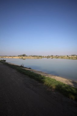 İtalya 'nın kırsal kesimlerinde güneşli bir günde ufuk çizgisi ve köprüsü olan küçük bir ada tarafından yapılan saptırıcı bir kanalda çatal.