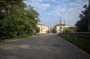 İtalyan kırsalındaki bir köyde caddeye çıkan ağaçlarla çevrili bir yol.