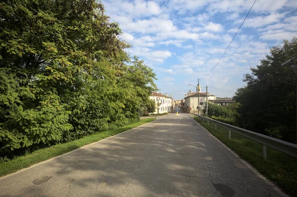 İtalyan kırsalındaki bir köyde caddeye çıkan ağaçlarla çevrili bir yol.