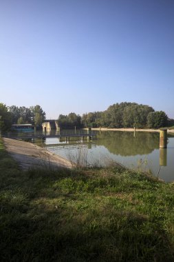 Kıyıların yanında demirleme direkleri ve güneşli bir günde İtalyan kırsalında ağaçlarla çevrili bir yol köprüsü olan saptırıcı bir kanal.