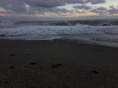 Gün batımında rüzgarlı bir günde kıyıda dalgalar eziliyor.