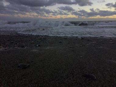 Gün batımında rüzgarlı bir günde kıyıda dalgalar eziliyor.