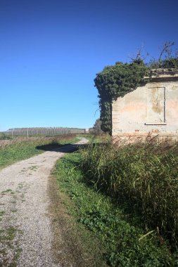 İtalya kırsalındaki bir patikanın kenarındaki çimenlikte terk edilmiş bir bina.