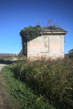 İtalya kırsalındaki bir patikanın kenarındaki çimenlikte terk edilmiş bir bina.