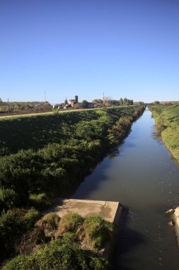 İtalya 'nın kırsal kesimindeki bir arazinin üzerinde ufuk çizgisi olan bir korulukla bir tarlanın yanındaki setler arasında küçük bir saptırma kanalı.