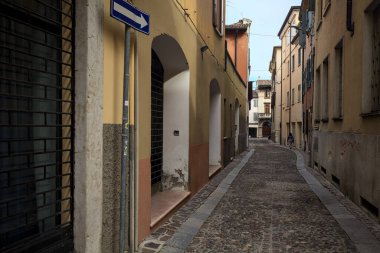 Üzerinde bulutlu bir gökyüzü olan dar dar bir sokak. İtalyan kasabasının ön cephesinde kapalı bir dükkan.