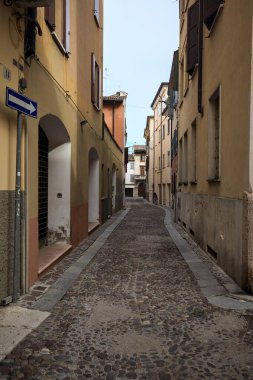 Üzerinde bulutlu bir gökyüzü olan dar dar bir sokak. İtalyan kasabasının ön cephesinde kapalı bir dükkan.