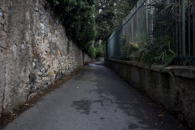 Bulutlu bir günde, İtalya 'nın bir şehrinde, taş bir duvarla bir bahçe çiti arasında dar bir sokak.