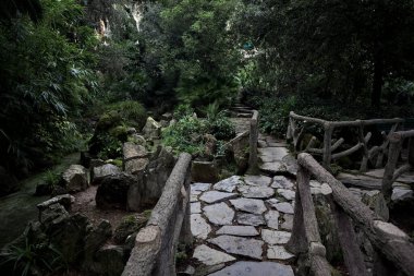 Taştan köprülü gölet ve parkın tenha bir bölgesinde gölgede ahşap raylar.