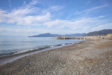 Güneşli bir günde kumsalda çakıl taşları ve arka planda kayalıklar vardı.