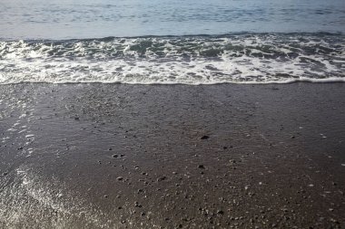 Kuma vuran dalgalarla kıyı şeridi ve güneşli bir günde ufukta durgun bir deniz.