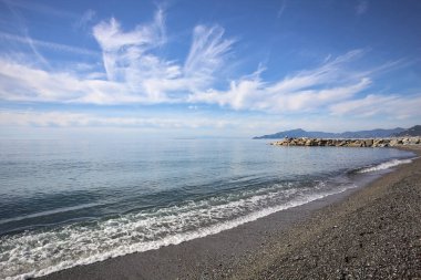 Güneşli bir günde kumsalda çakıl taşları ve arka planda kayalıklar vardı.