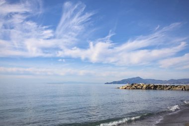 Güneşli bir günde kumsalda çakıl taşları ve arka planda kayalıklar vardı.