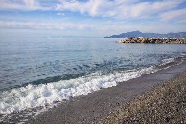 Güneşli bir günde kumsalda çakıl taşları ve arka planda kayalıklar vardı.